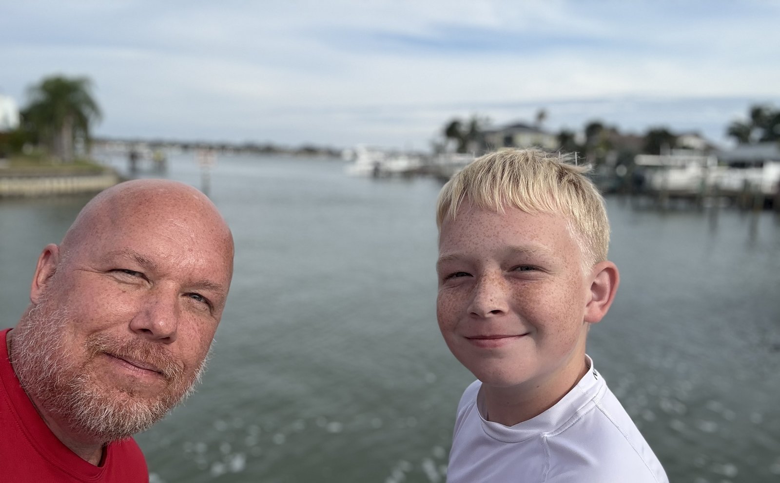 Chris Naylon and his younger son grinning in a selfie by the water on a cloudy afternoon.
